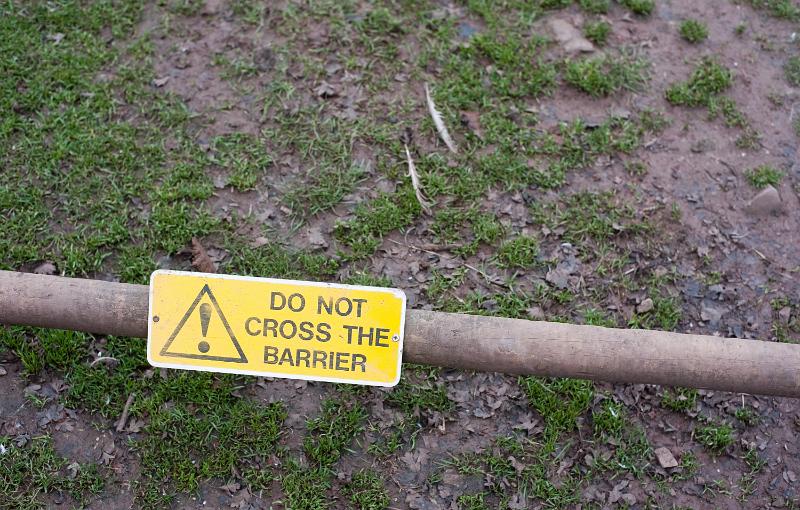 Free Stock Photo: Yellow warning sign - Do Not Cross This Barrier with exclamation mark mounted on an iron pole overlooking a patch of grass