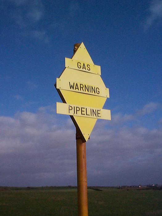 Free Stock Photo: Gas pipeline warning sign in countryside with black letters on yellow background on the pole in the field. Viewed from low angle against cloudy sky