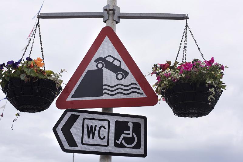Free Stock Photo: Quayside warning sign on a metal pole with hanging baskets of summer flowers and WC sign for handicapped people