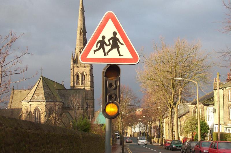 Free Stock Photo: Traffic light below a school warning sign in a town street at dusk with old stone church with tall steeple