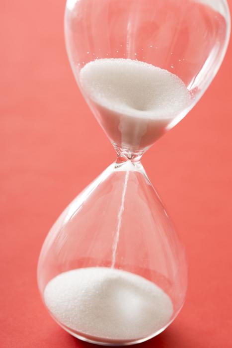 Free Stock Photo: White sand running through an hourglass or egg timer measuring passing time counting down to the end or a deadline over a red background