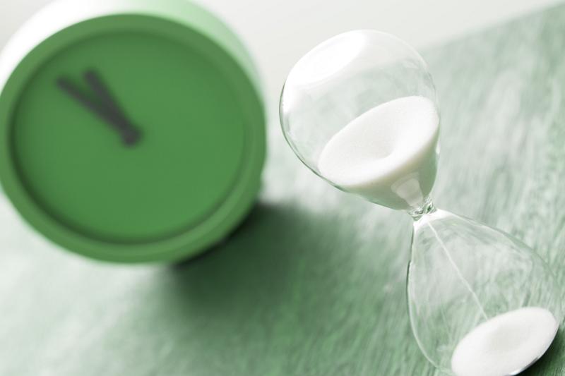Free Stock Photo: Green timer clock and egg timer used for cooking or counting down to a deadline over a green background in a tilted angle view