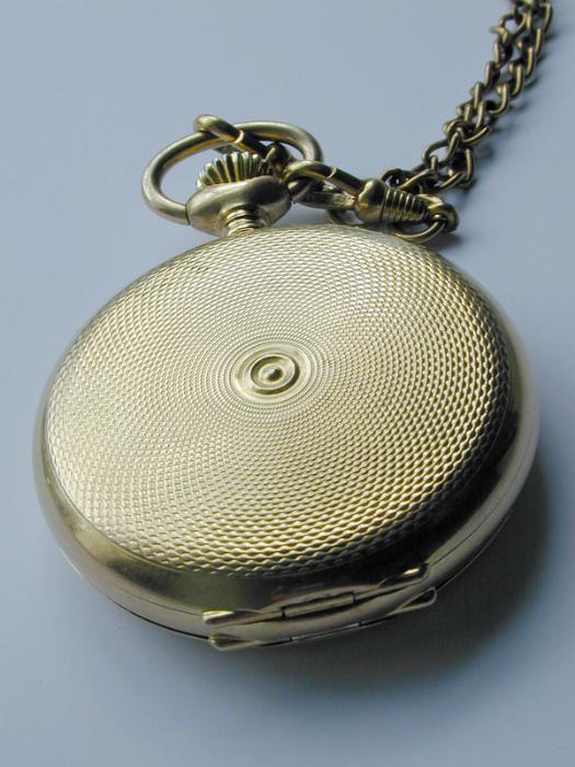 Free Stock Photo: Closed vintage full hunter pocket watch with a tooled and engraved case and chain, closeup high angle view showing the texture of the embossing