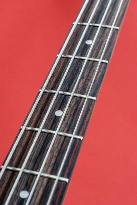 Free Stock Photo: the neck, strings and frets on a bass guitar pictured against a red background