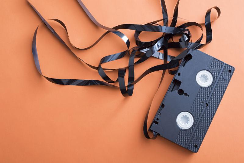 Free Stock Photo: Damaged video cassette with uncoiled tape in a tangled mess over an orange background with copy space in a communications and entertainment concept