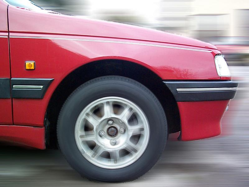 Free Stock Photo: Front side panel and tyre of a moving red car driving on a street in a close up view of the bodywork
