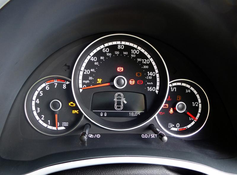 Free Stock Photo: Cluster of car instruments on a dashboard with a speedometer, warning light and fuel gauge on round dials on black trim