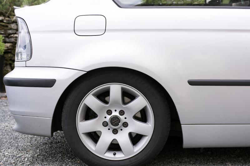 Free Stock Photo: Close up of rear car wheel on white automobile parked in driveway by bushes