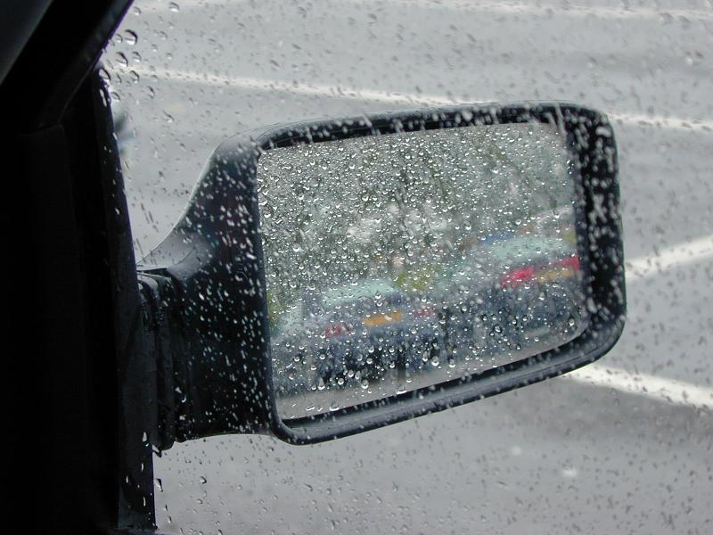 Free Stock Photo: Viewing a car side view mirror in the rain through the passenger window covered in condensed raindrops