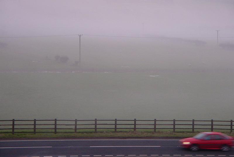Free Stock Photo: Side view of a red sedan car driving on a rural motorway with fog obscuring the landscape and reduced visibility