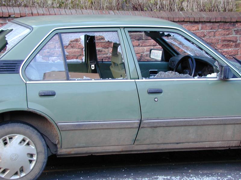 Free Stock Photo: Old green car with smashed passenger windows form vandalism or an accident parked in front of a brick wall with shards of glass on the ground