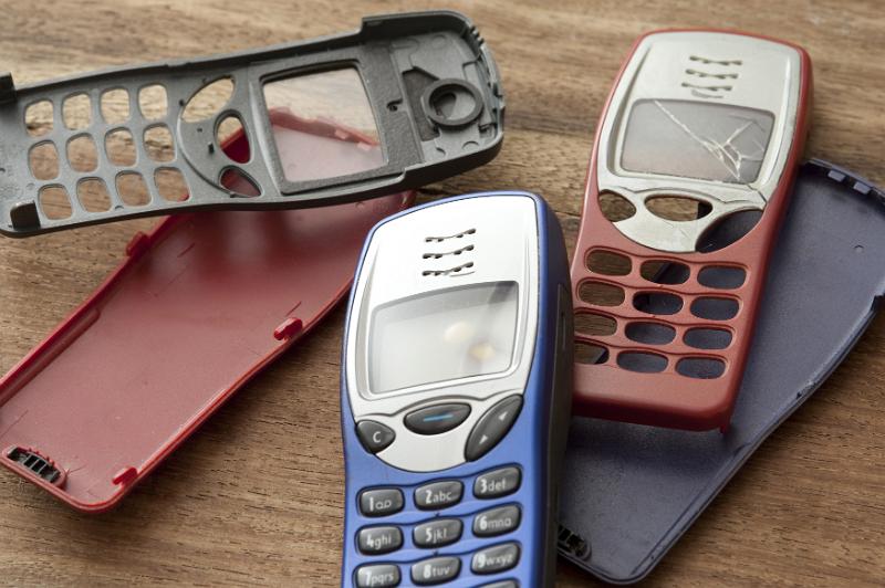 Free Stock Photo: Collection of colorful mobile phone covers from retro push button devices lying on a wooden table, one with a smashed screen