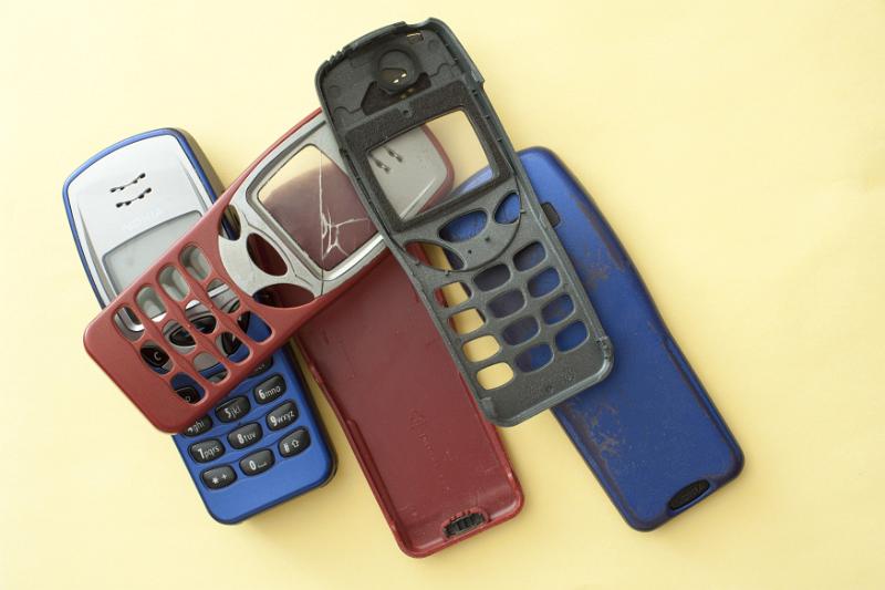 Free Stock Photo: Old loose red, black and blue covers for mobile phones with a button design, one with a cracked screen on a yellow background
