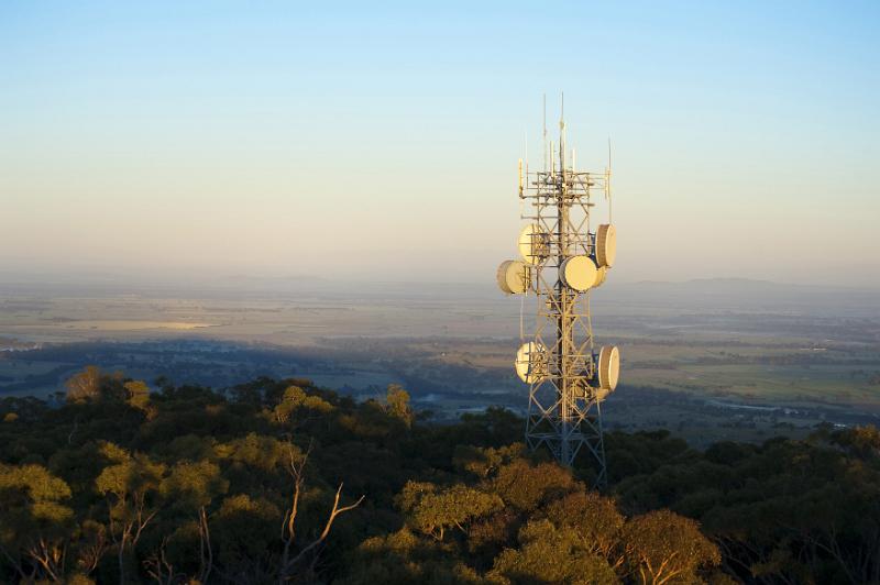 Free Stock Photo: Mobile phone communications mast on a forested hilltop with dish antennae in an open landscape at sunset