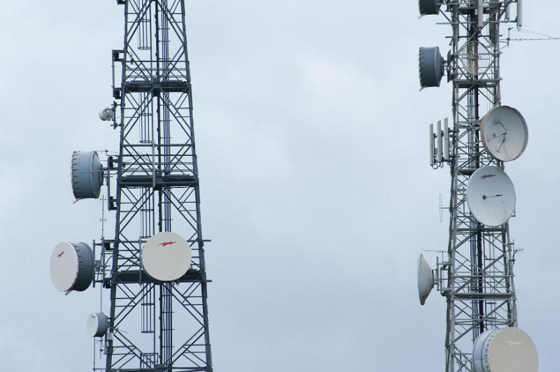 Free Stock Photo: Two mobile phone masts with dish antennae for transmitting and receiving radio signals in a communications concept close up against a grey cloudy sky