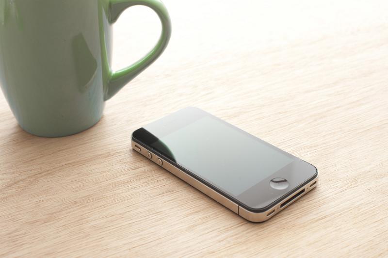 Free Stock Photo: Blank mobile phone lying alongside a mug of coffee on a wooden table in a communication concept