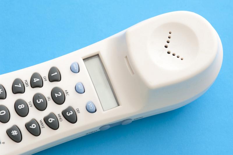 Free Stock Photo: Close up of a land line phone keypad on a white handset receiver lying on a blue background in a communications concept