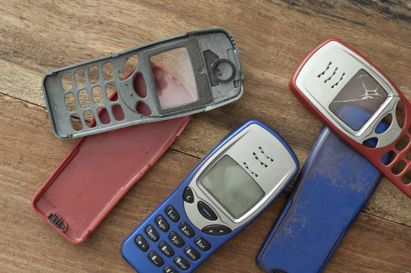 Free Stock Photo: Assorted red, blue and black cases or covers for a retro button style mobile phone or cellphone lying loose on a wooden table, some with cracks and damage - not property released