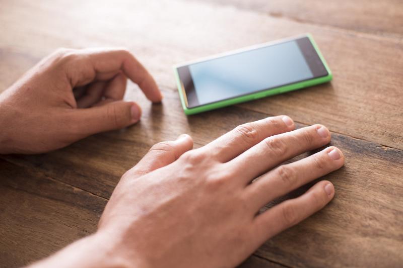Free Stock Photo: Close up of a mans hands as he taps on a wooden table anxiously while waiting for a call on a smart phone.