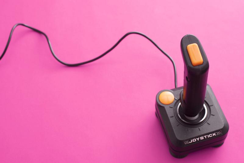 Free Stock Photo: Retro black and orange joystick over pink background with copy space. Cord reaching around top side.