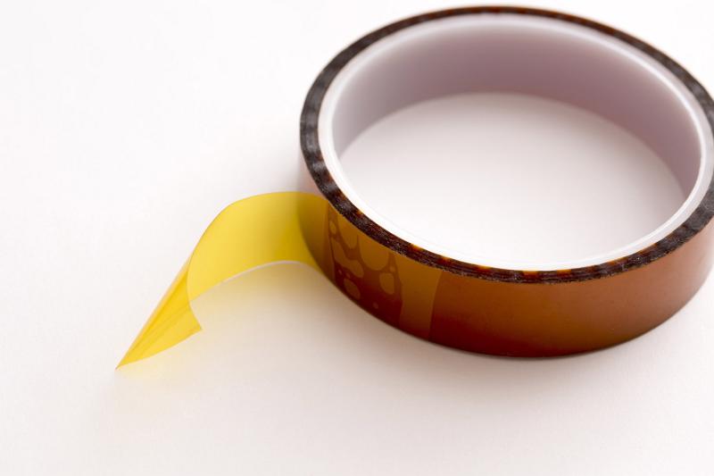Free Stock Photo: Roll of yellowish Kapton tape with end detached close-up on white table surface