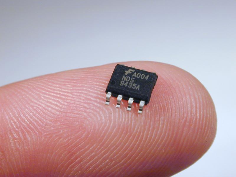 Free Stock Photo: Small black integrated circuit chip on tip of a finger - macro detail view on grey background