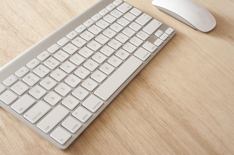 Free Stock Photo: slimline wireless computer keyboard and while coloured mouse on a wooden table top