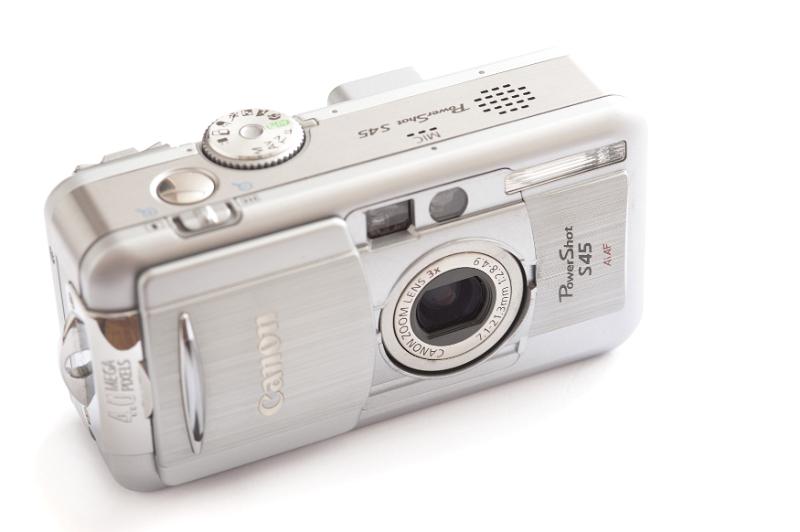 Free Stock Photo: Old Canon Power Shot S45 silver digital compact camera with a slide to cover the lens viewed from the front high angle on white