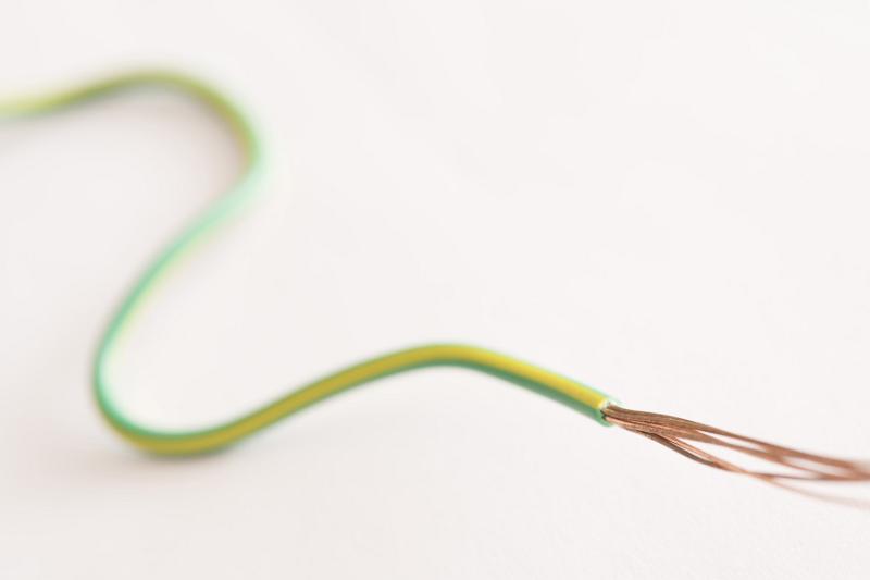 Free Stock Photo: Snaking piece of green and yellow plastic coated and coded earth wire with splayed copper ends over white with copy space