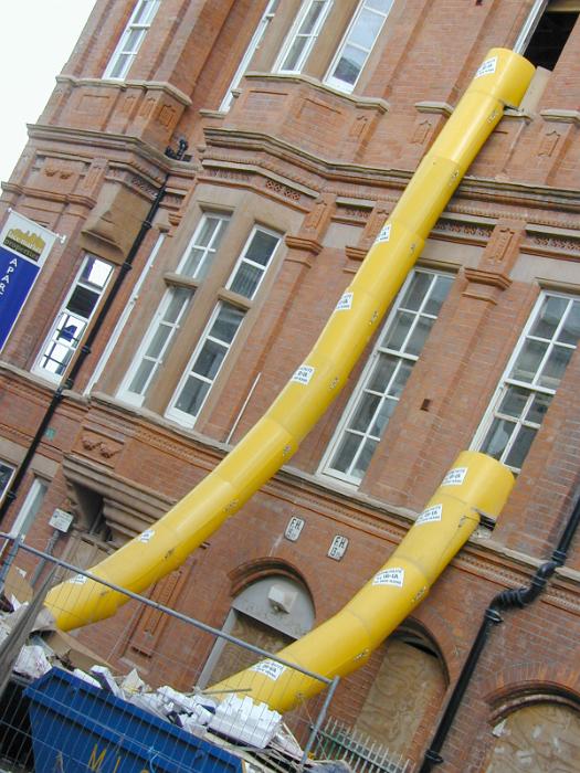 Free Stock Photo: Renovation construction on an old red brick building with external chutes to dispose of building waste reaching down to a tip on the ground to