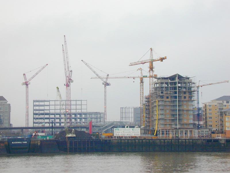 Free Stock Photo: Constructing site with a lot of office and residential buildings under construction and many cranes on the bank, viewed from the water against smoky grey sky