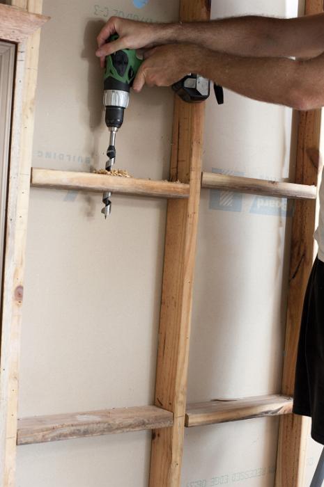 Free Stock Photo: Man drilling wire hole in stud wall with a battery drill, holding it with both hands