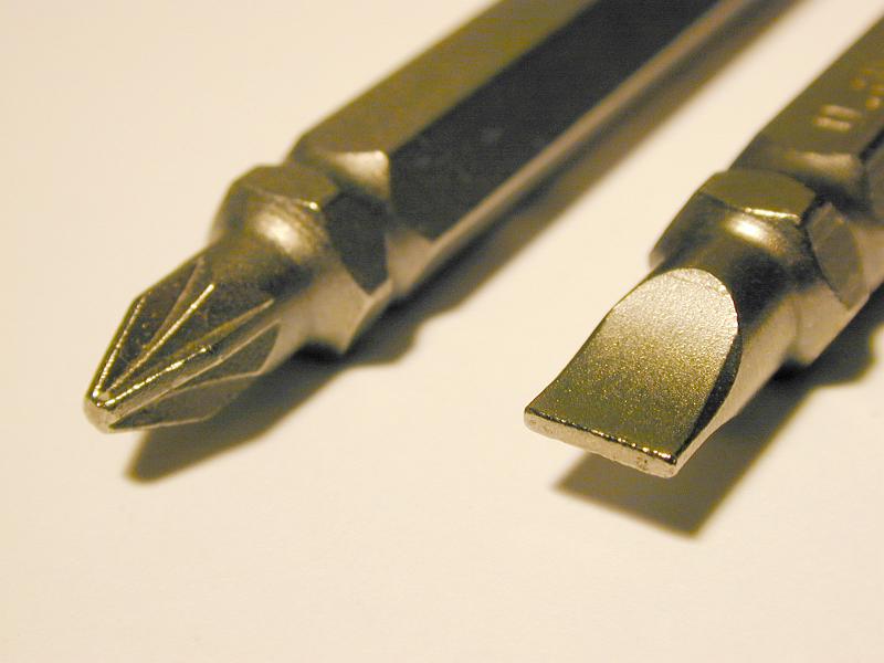 Free Stock Photo: Two metal screwdriver bits, a Phillips and slot head, on a white background with shadow and copy space