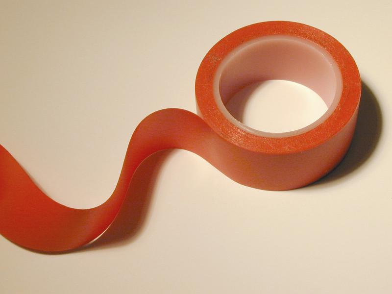 Free Stock Photo: Red electric insulation tape with unrolled wavy end in close-up on white table