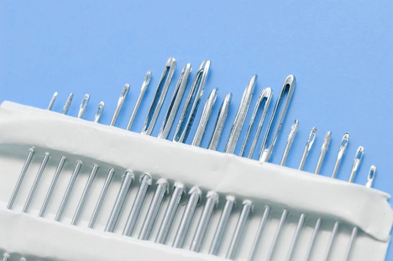 Free Stock Photo: Set of different sized sewing needles in white holder over blue background