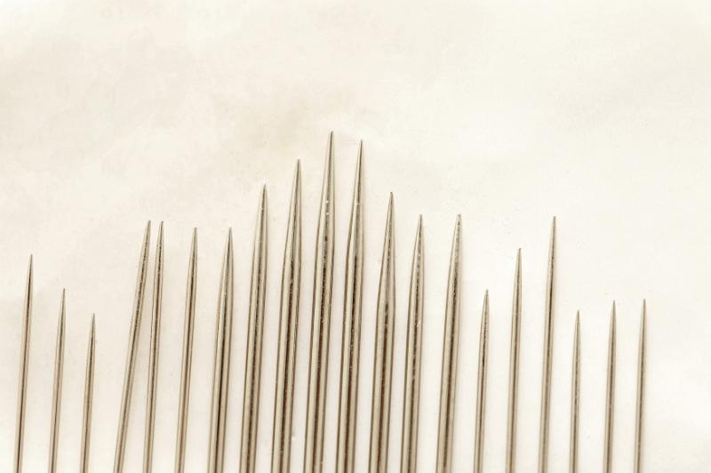 Free Stock Photo: Close up on set of various sized sewing needle points organized by height and thickness over paper