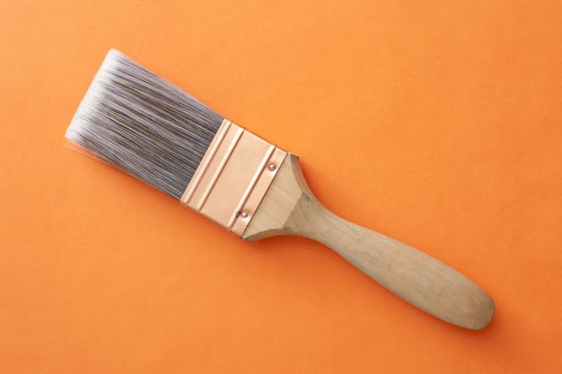 Free Stock Photo: Clean new interior decorating paint brush with fine bristles and a wooden handle lying diagonally on an orange background with copy space