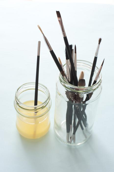 Free Stock Photo: One dirty paint brush in cleaning solution next to jar full of various sized tips over white background with shadow