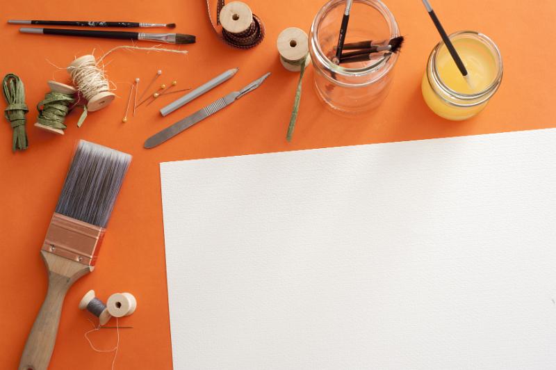 Free Stock Photo: Blank paper surrounded by paint brushes, spools, thread, wire, blades and pins over orange background