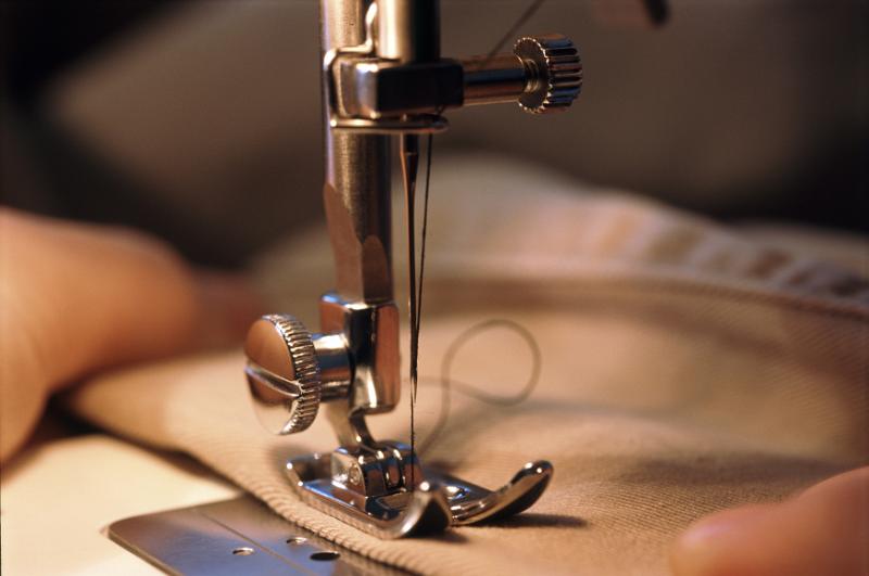 Free Stock Photo: Extreme close up of hands pushing brown fabric through sewing machine needle head