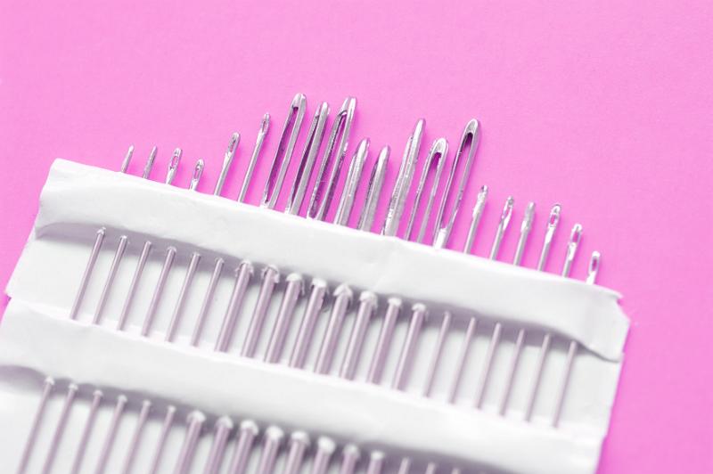 Free Stock Photo: Close up on set of various sized sewing needle points in paper package organized by height and thickness over pink background