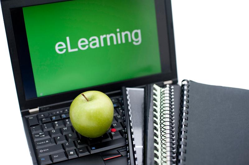 Free Stock Photo: E-learning or distance learning concept with spiral bound notebooks and a fresh green apple lying on the keyboard of an open laptop with the word eLearning visible on the screen