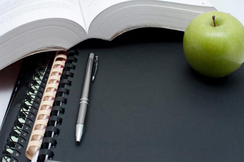 Free Stock Photo: Education and learning background with a fresh healthy green apple alongside an open book with a pen and spiral binders