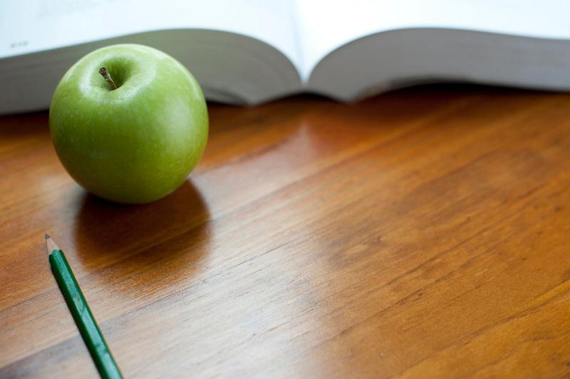 Free Stock Photo: Fresh green apple with an open textbook and pencil on a wooden desktop in an educational concept with copyspace