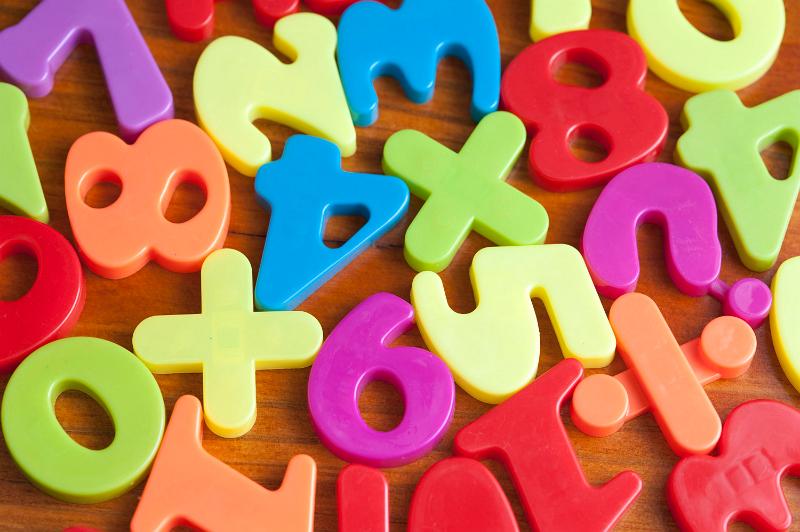 Free Stock Photo: Close up showing fridge magnets of numbers and mathematical symbols, in bright colours over wood effect background