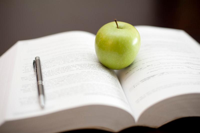 Free Stock Photo: A fresh juicy green apple stands on an open textbook with a pen conceptual of education and learning