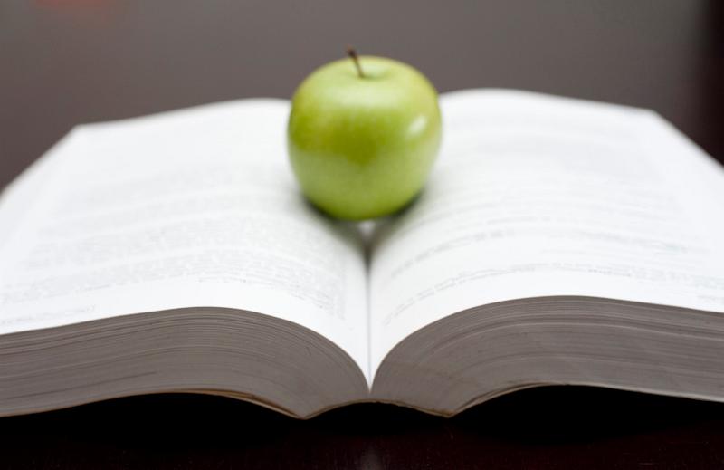 Free Stock Photo: Fresh green apple balanced on the open pages of a textbook or novel in an education and learning or relaxation and reading concept