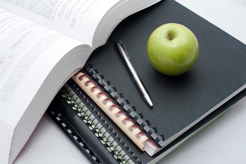 Free Stock Photo: Conceptual background for school reading and studies with a fresh juicy green apple and pen lying on spiral bound notebooks alongside an open book