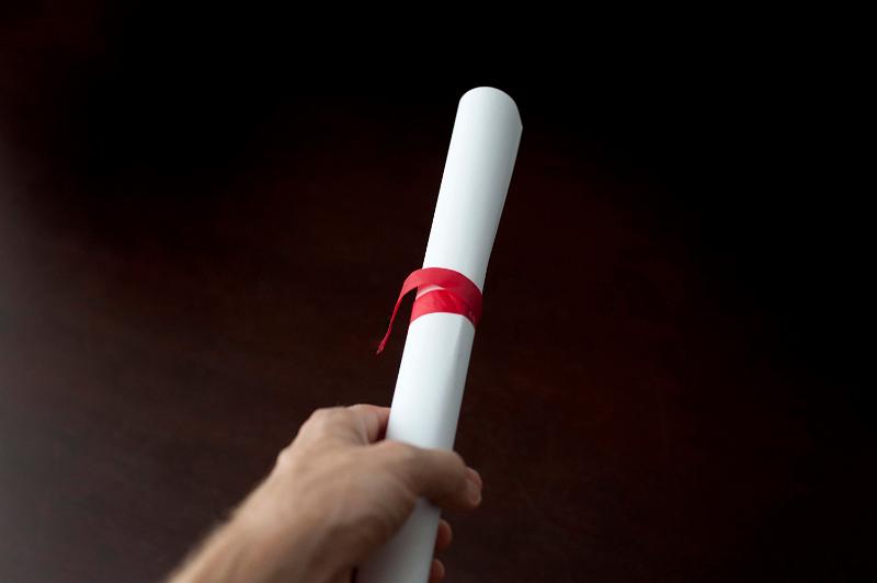 Free Stock Photo: Studio shot over black of a a male hand holding a diploma or document, rolled and tied with red ribbon