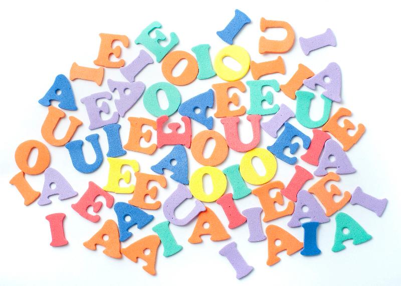 Free Stock Photo: Collection of plastic vowels scattered randomly on a white surface for use in teaching children basic language and grammar and to read, write and spell
